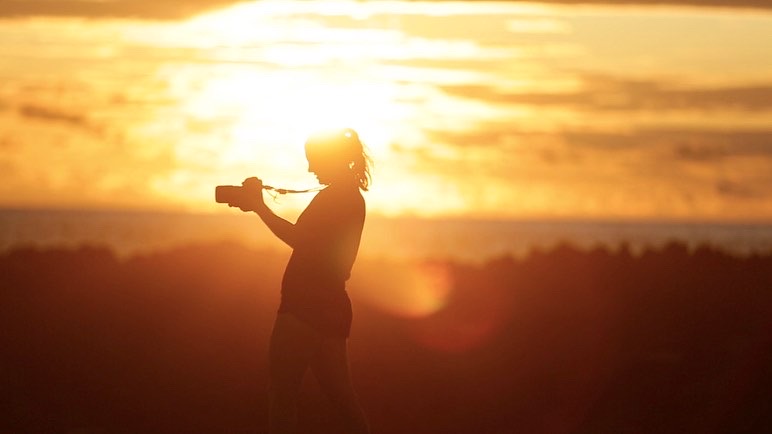 Renata stands silhouetted by golden light holding her camera.